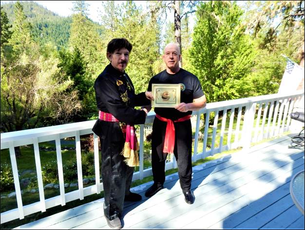 Two men standing on a white railing holding a certificate  Description automatically generated